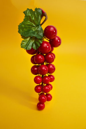Decorative red bunch of grapes with green leaves isolated on yellow background.の写真素材