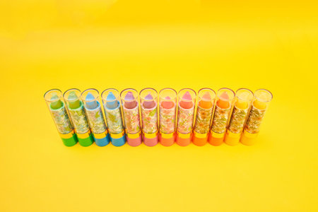 A row of multi color lipsticks with floral pattern isolated on the yellow background. Essential...