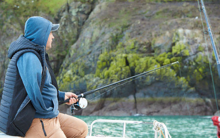 fisherman is fishing in open sea from the boat on the island background.