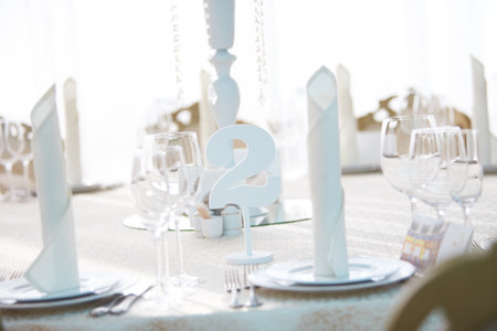 Festive table in the banquet hall are decorated with plates, glasses and cards for guests.