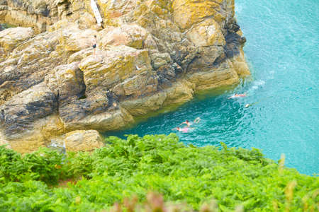 A group of guys swimming in the sea near the cliff on the blue ocean waves with green grass hills.の写真素材