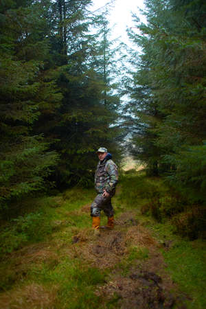 A hunter in the forest during the day with moss and grass.