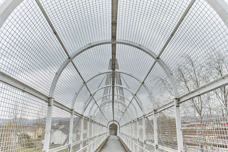 A long pedestrian tunnel with metal arches and mesh design. Aerial pedestrian crossing over the highway, perspective goes to the horizon, a empty tunnel no peopleの写真素材
