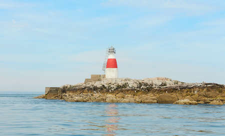 Old Muglins Lighthouse on the isolated island the backdrop of the blue cloudy sky.の写真素材