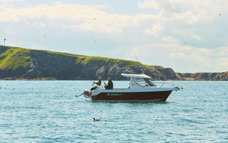 Dublin, Ireland - 05.26.2021: Fishing boat on the sea with island in background. Glitter sea water.