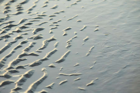 Sand waves texture with water on the sea beach. Yellow sand texture for background.