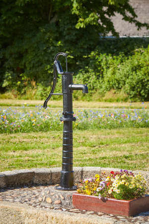 Old black street water pump. Usually the water from such pumps is not potable. In the background street and buildings painted in different colors.