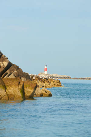 Old Muglins Lighthouse on the isolated island the backdrop of the blue cloudy sky.