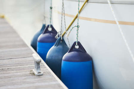 White fenders suspended between a boat and dockside for protection. Maritime fendersの写真素材