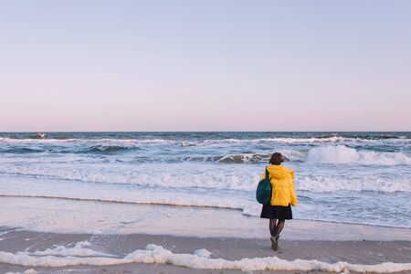 A girl in a skirt with a backpack stands alone in front of the seaの写真素材