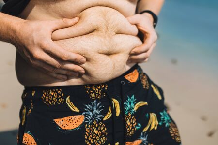 Young man crumples his fat belly on the sea in summer in Asiaの写真素材