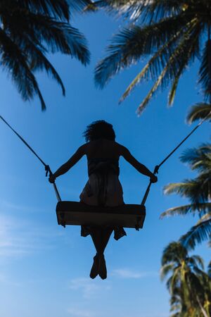Girl flies away on a swing to palm trees by the seaの写真素材