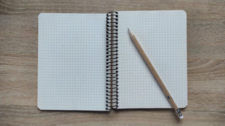 Open spiral notebook with squared grid paper and wooden pencil on a light wooden table. Minimal...