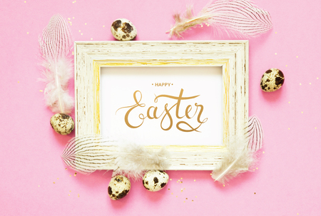 Inscription Happy Easter. Easter composition with easter eggs and feathers on pink background.の写真素材