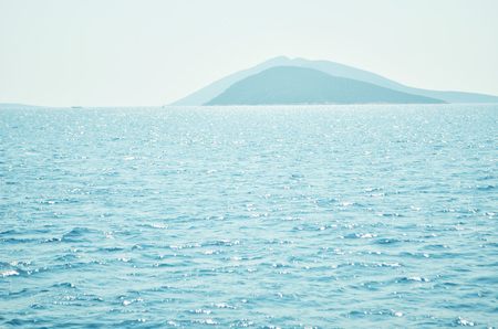 Sea water surface and waves stretch out to the horizon where islands are visible far away.の写真素材