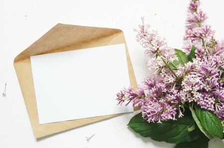 Lilac flowers and envelope on white background. Spring flowers. Top view, flat lay. Copy space. -...