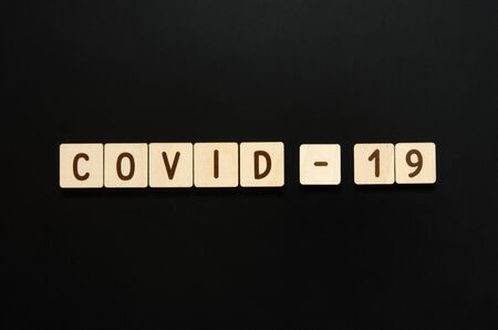 COVID-19 - words from wooden blocks with letters. Top view on black background. - Imageの写真素材