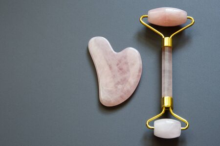 Pink Gua Sha massage tool on a gray background. Rose Quartz roller. Facial skin care at home, anti-aging and lifting therapy. Top view. - Imageの写真素材