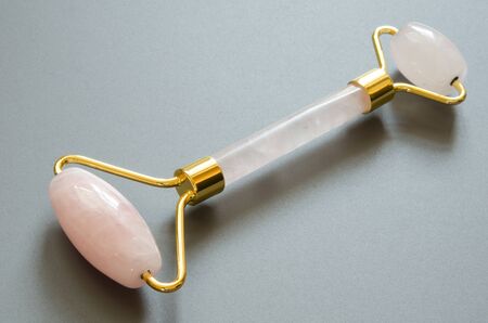 Pink Gua Sha massage tool on a gray background. Rose Quartz roller. Facial skin care at home, anti-aging and lifting therapy. - Imageの写真素材