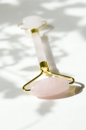Pink Gua Sha massage tool. Rose Quartz roller. Gray shadow of the leaves on a white background. Facial skin care at home, anti-aging and lifting therapy.  - Imageの写真素材