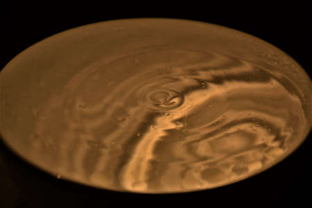 Water drops splashing into bright gold reflected water shapesの写真素材