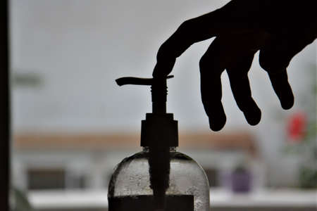 A person using hydroalcoholic disinfectant gel from a bottle onto his hand. Backlight from the sun. Persons hands with liquid falling from the bottle.の写真素材