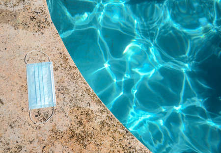Blue face mask for protection against the Corona Virus (COVID-19), laying beside a swimming pool during coronavirus worldwide pandemic holidaysの写真素材