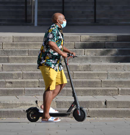 Barcelona, Spain, August 24, 2020: African man wearing protective covid-19 face mask while riding his electrical scooter. Touristy spots in the covid eraのeditorial素材