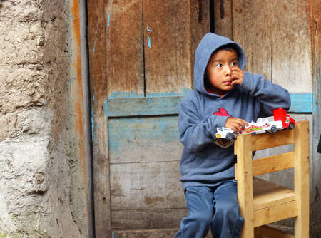 Cuenca, Ecuador - October 7, 2018: Small ecuadorian boy from poor village family sitting in the courtyard of the house and playing with toy car. Cuencaのeditorial素材