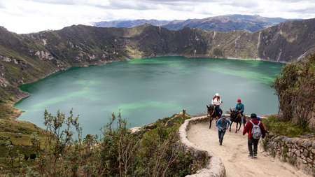Quilotoa, Ecuador - April 16, 2022: Lake Quilotoa in caldera of eponymous volcano. Hiking patch and tourists riding horses to up the hill. Cotopaxi province, Ecuadorのeditorial素材