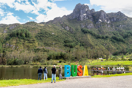 Azuay province, Ecuador - May 29, 2022: People relax at the recreation area on the mountain lake Busa. Sign of lake's name 'Busa' on the shore lake. Mountain San Pablo at the backgのeditorial素材