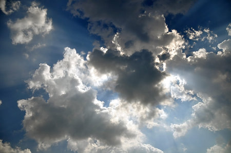 The sun s rays coming out from behind the clouds on a blue sky