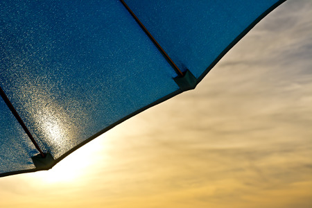 Fragment of a blue garden umbrella against the sky with clouds.の写真素材