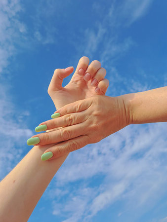 women's hands on the background of a summer blue sky with cloudsの写真素材