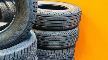 Stack of black car tires against a bright orange wallの写真素材