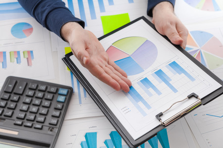 Businessman holding a pen is working with graph documents and sunset light background. Stock market chart and finger pointing on tablet in office.の写真素材