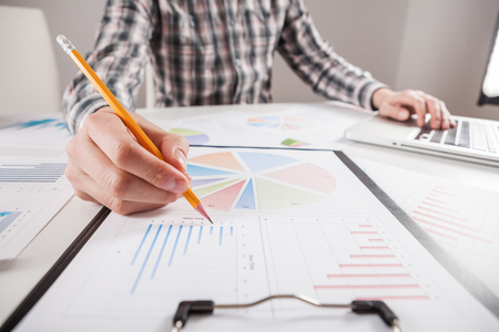 Businessman holding a pen is working with graph documents. Stock market chart and finger pointing on tablet in office.の写真素材