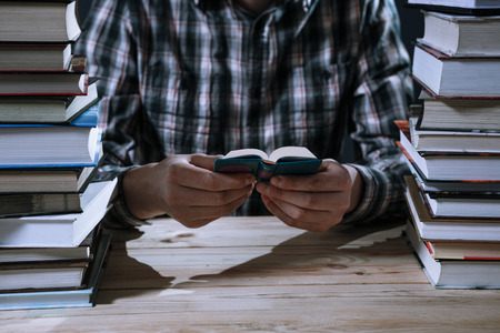 A man reading a miniature book among the big books in the library at the wooden table.の写真素材