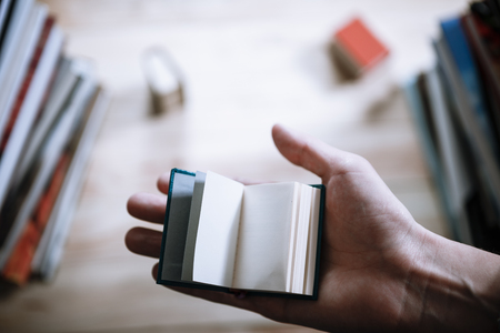 A man reading a miniature book among the big books in the library at the wooden table.の写真素材