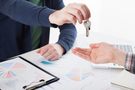Young business man giving house with keys of customer at agency officeの写真素材