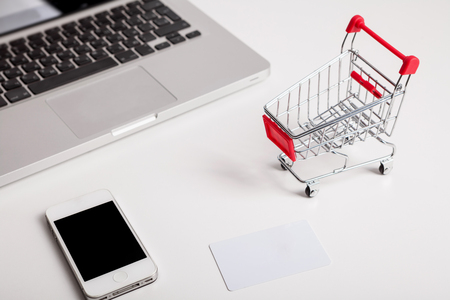 Online shopping. Bank card nearby a laptop and mini shopping cart on white background top view. の写真素材