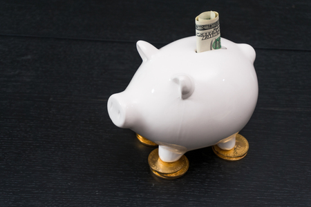 White piggy bank with one gold bitcoin coin new virtual money on a colored wooden backgroundの写真素材