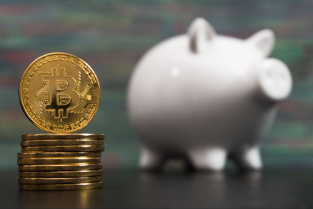 White piggy bank with one gold bitcoin coin new virtual money on a colored wooden backgroundの写真素材