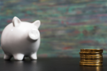 White piggy bank with one gold bitcoin coin new virtual money on a colored wooden backgroundの写真素材