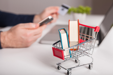Online purchase of books. Bank card nearby a laptop and mini shopping cart on white background top view.の写真素材