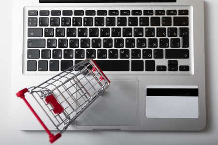 Online shopping. Bank card nearby a laptop and mini shopping cart on white background top view.の写真素材