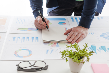Businessman holding a pen is working with graph documents and sunset light background.の写真素材