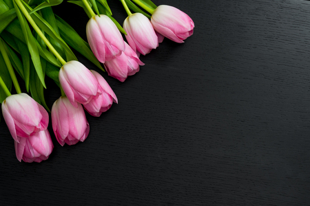 Border from bright pink tulips flowers on black wooden background. Selective focus. Place for text. Flat lay.の写真素材