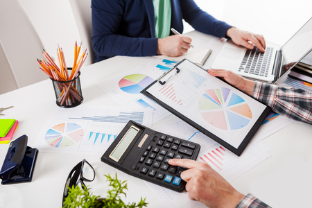 Business people discussing the charts and graphs showing the results of their successful teamwork.  Stock market chart and finger pointing on tablet in office.の写真素材