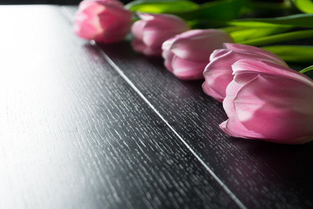 Border from bright pink tulips flowers on black wooden background. Selective focus. Place for text. Flat lay. With an artificial Sun Reflexの写真素材